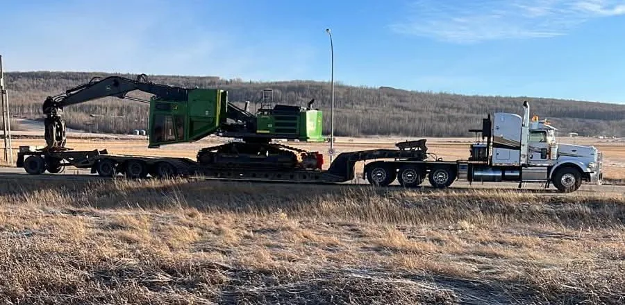 Tractor hauling a tracked feller buncher on a double drop low bed trailer