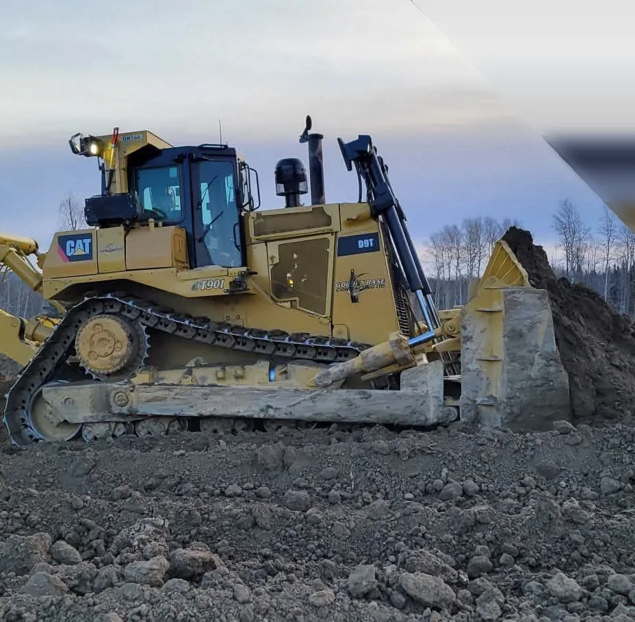 Large tracked dozer with a full blade of soil pushing spoil on a pad at dusk