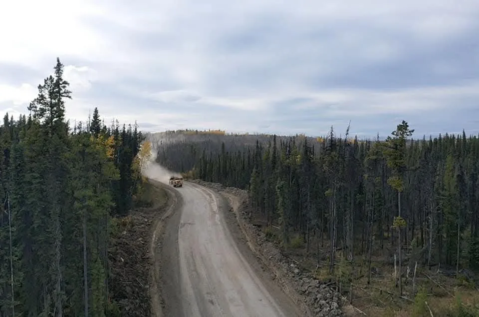 Rock truck raising dust on a gravel haul road cut through spruce