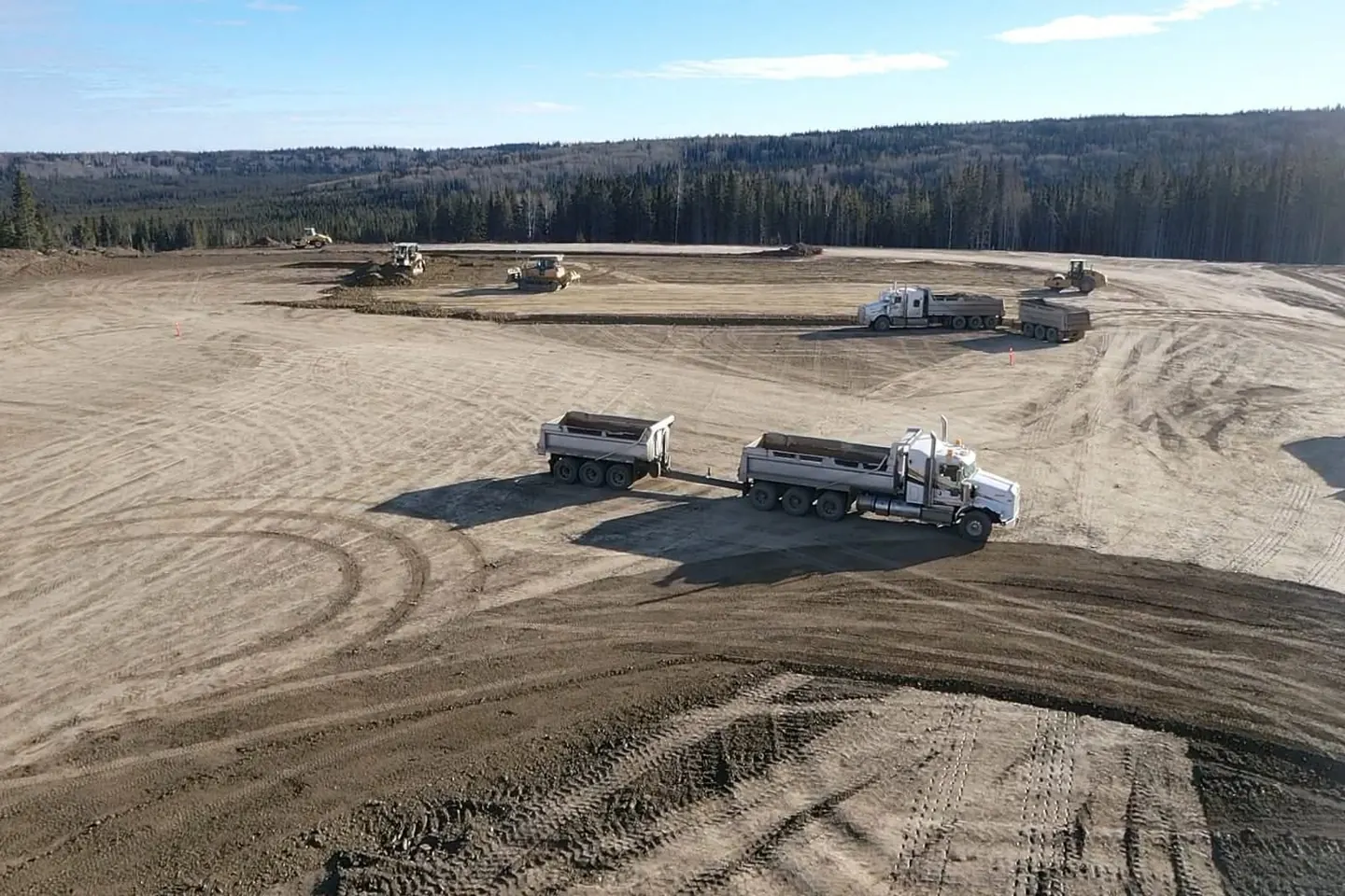 Two truck and pup end dump units working a graded pad with dozers behind them