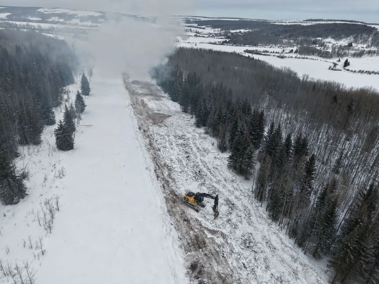 Aerial view of an excavator clearing a right of way through snow covered forest