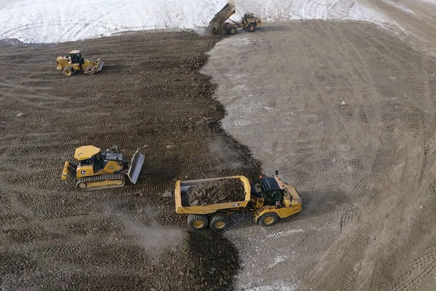 Rock truck placing fill while a dozer and packer work the lift behind it