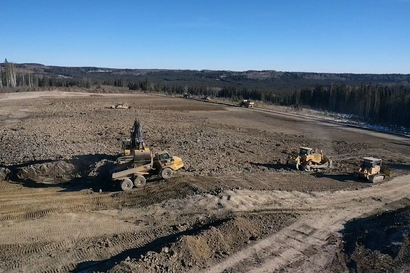 Wide aerial view of excavators, rock trucks and dozers working a pad build