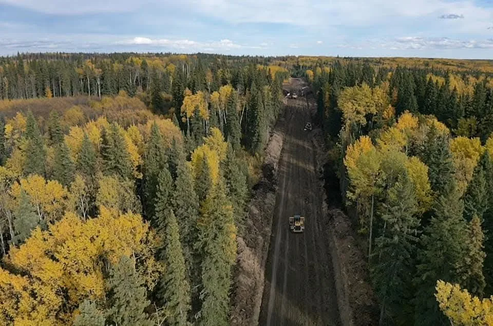 Aerial view of a dozer grading a newly cut right of way through mixed forest in autumn