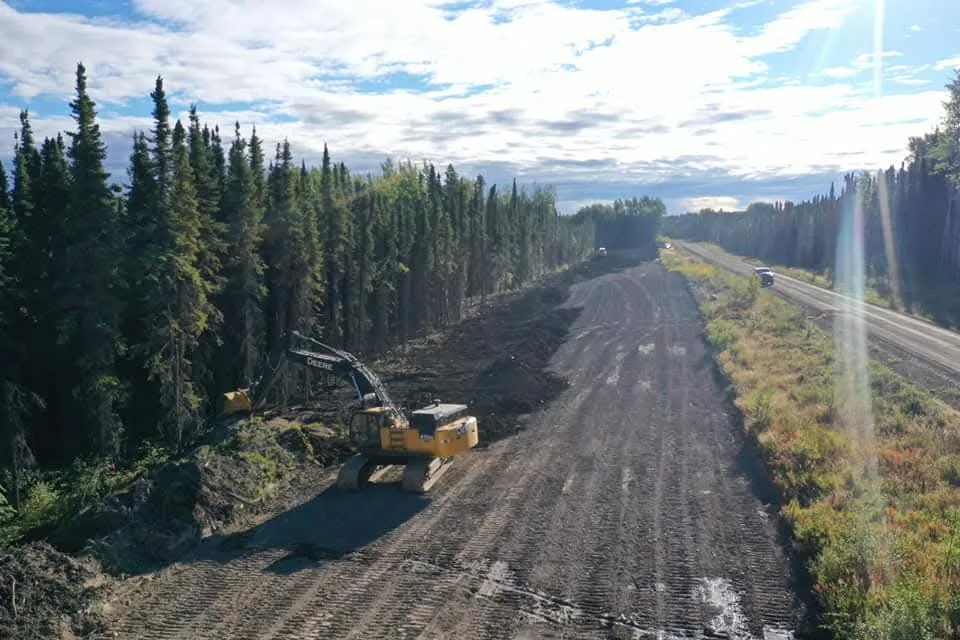 Tracked excavator with a mulching head working the shoulder of a wide dirt road