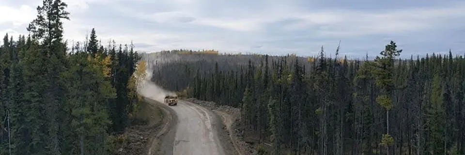 Rock truck raising dust on a gravel haul road cut through spruce