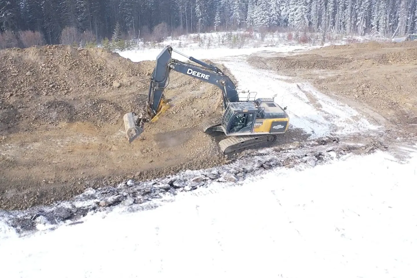 Deere 350G excavator digging into a cut face beside a snow covered access road