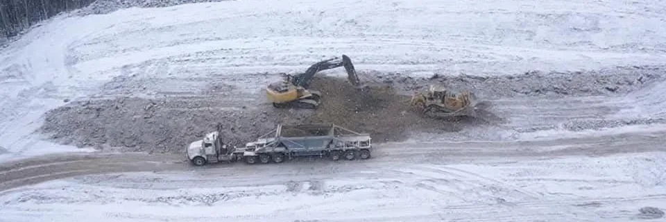 Excavator, dozer and end dump working a snow-covered pad