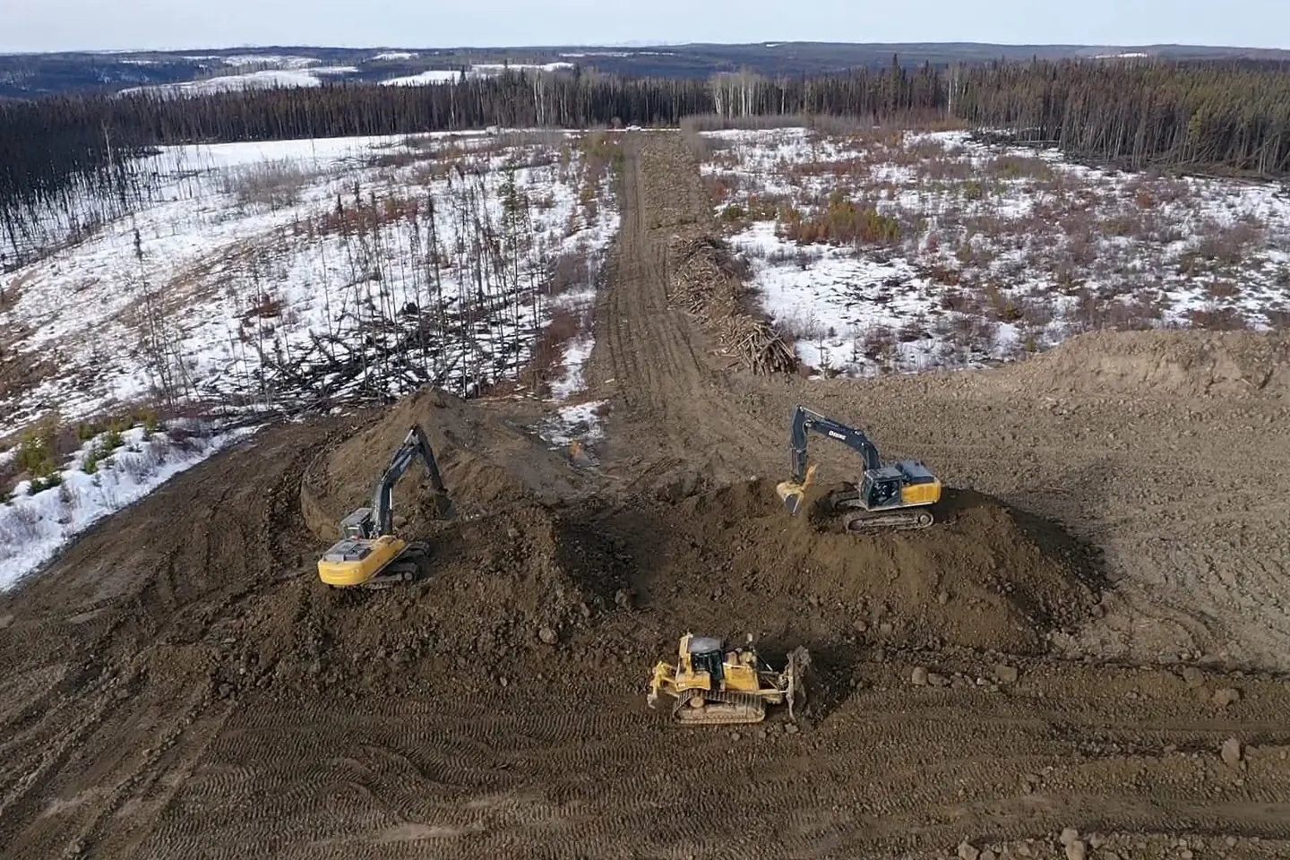 Aerial view of two excavators and a dozer building a cleared right of way in snow