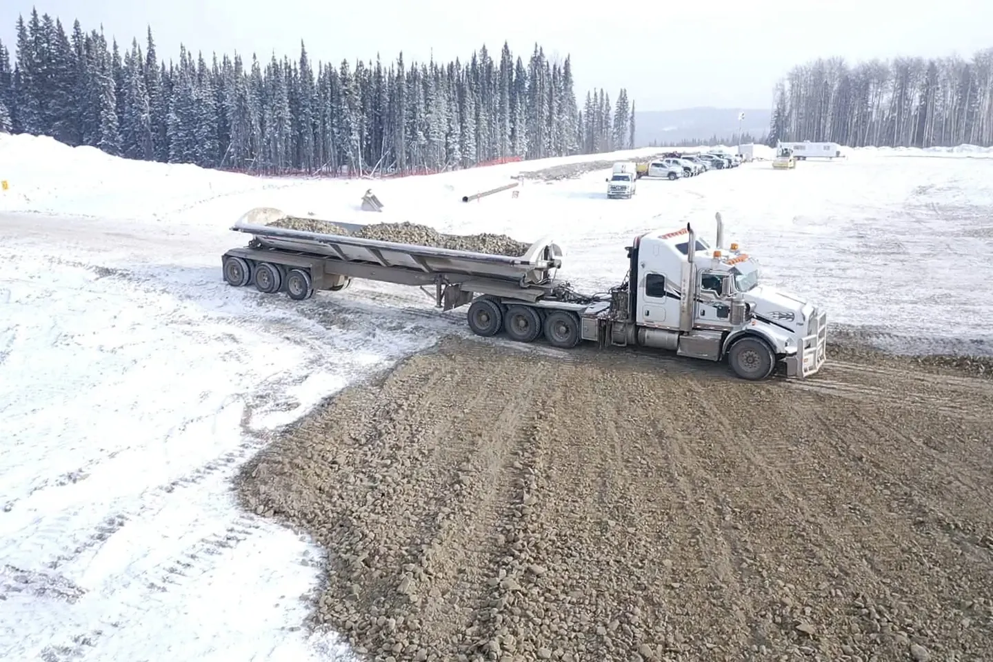 Kenworth tractor and belly dump trailer spreading gravel on a snow covered road
