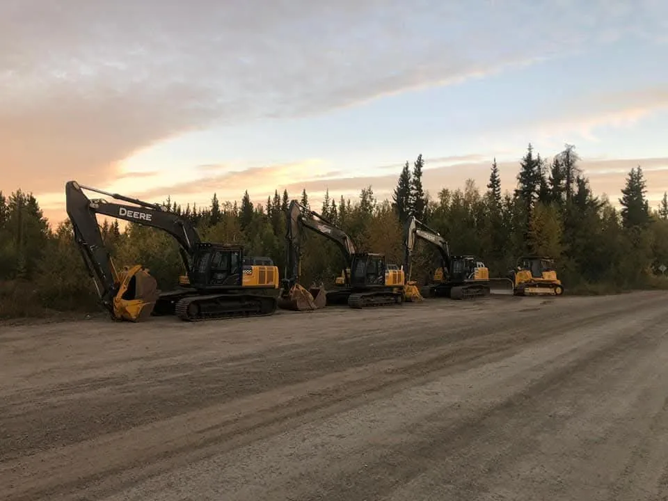 Row of tracked excavators and a dozer parked along a gravel road at sunset