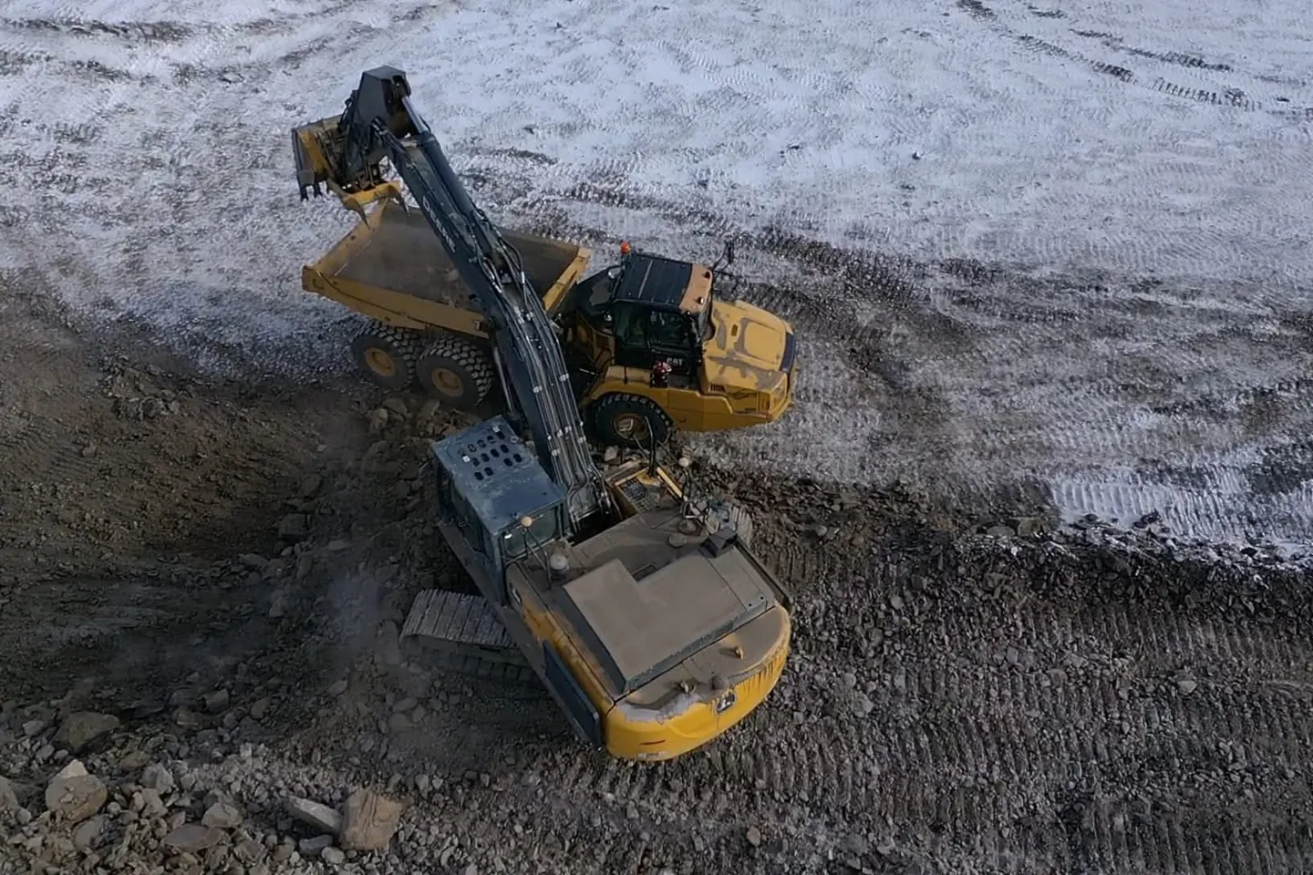 Excavator loading an articulated rock truck from a frozen cut face