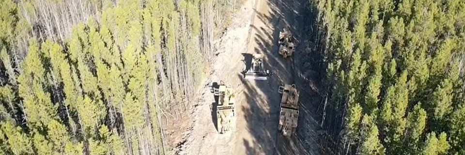 Aerial view of feller bunchers and skidders working a narrow cut line through young pine