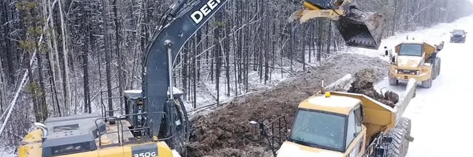 Tracked excavator loading articulated rock trucks alongside a trench in fresh snow