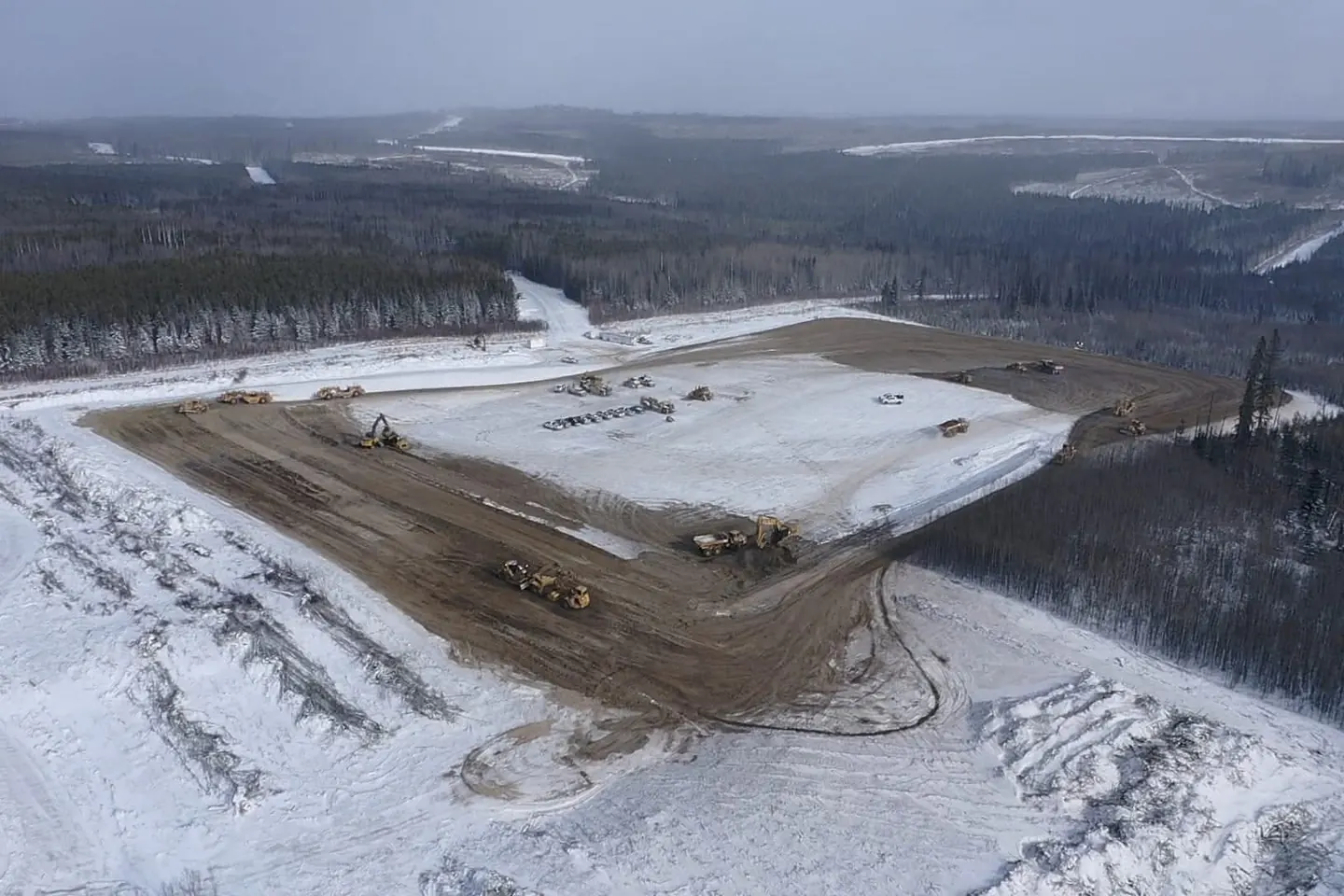 Aerial view of a snow covered pad with scrapers and rock trucks moving fill