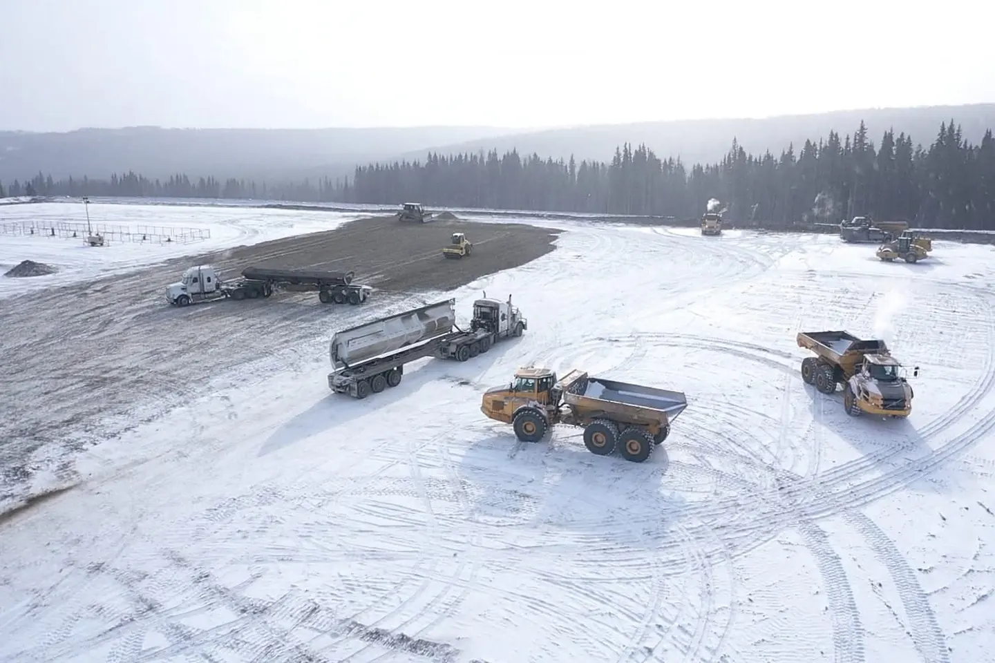 End dump units, articulated rock trucks and a packer working a snow covered pad