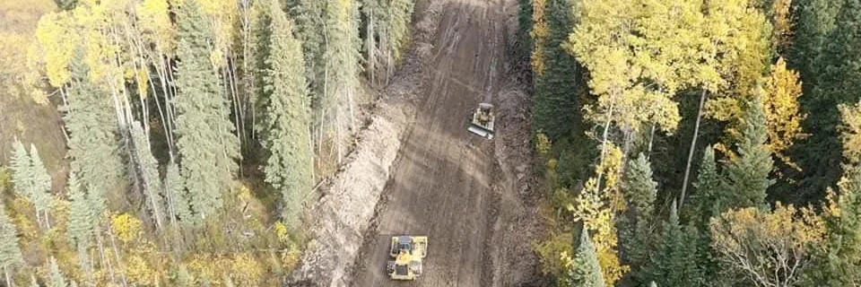 Aerial view of two dozers grading a freshly cut corridor through autumn forest
