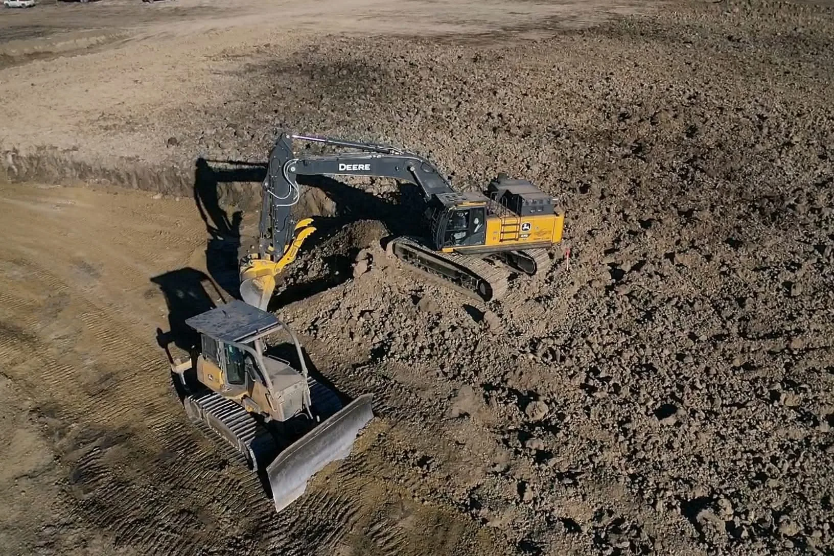 Aerial view of an excavator and a dozer cutting into a rock face on a pad