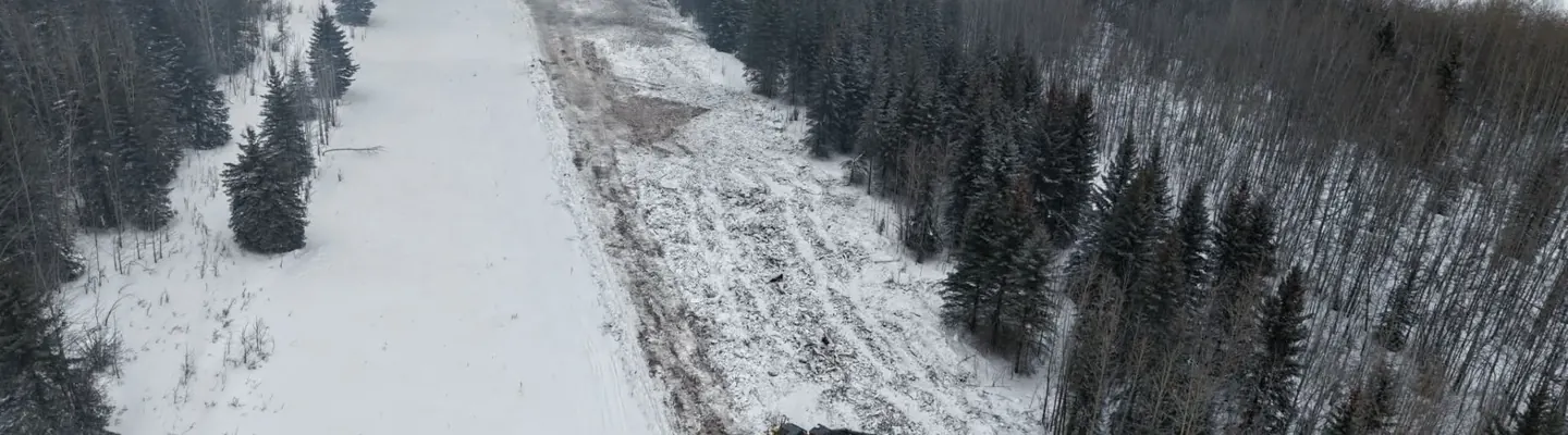 Aerial view of an excavator clearing a right of way through snow covered forest
