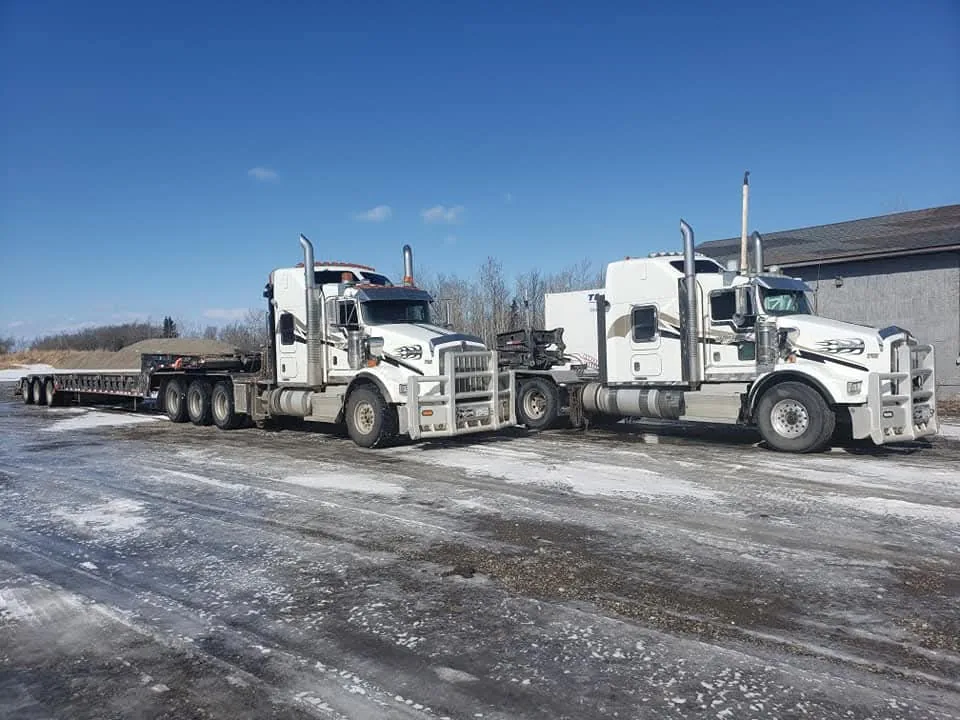 Two Kenworth tractors coupled to low bed trailers parked on an icy yard