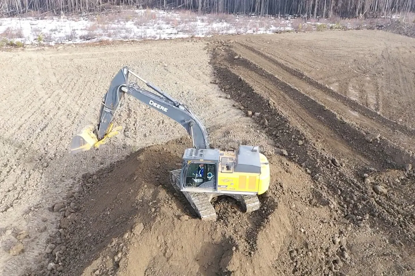 Deere excavator stripping topsoil into windrows on a pad