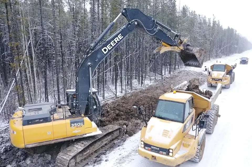 Tracked excavator loading articulated rock trucks alongside a trench in fresh snow