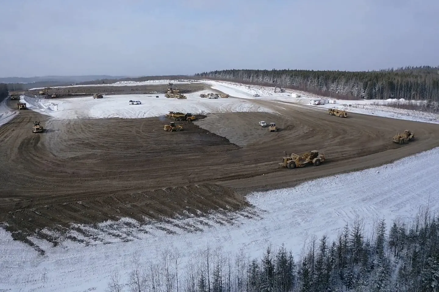 Wide view of scrapers and packers building a large pad in winter