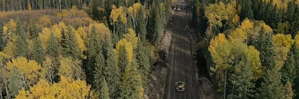Aerial view of a dozer grading a newly cut right of way through mixed forest in autumn