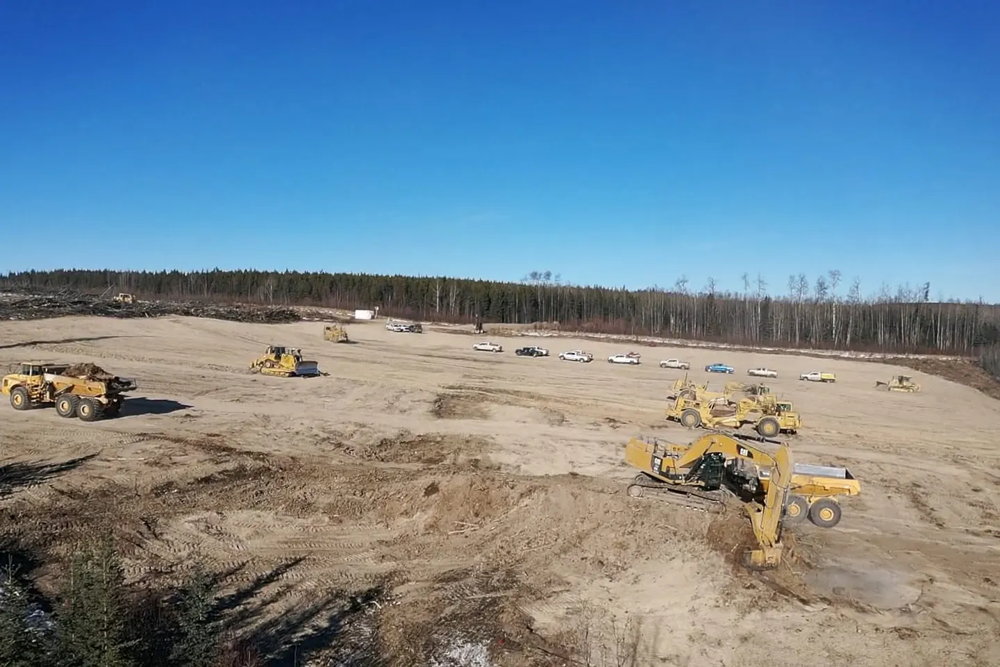 Scrapers, dozers and a rock truck spread across a wide graded pad