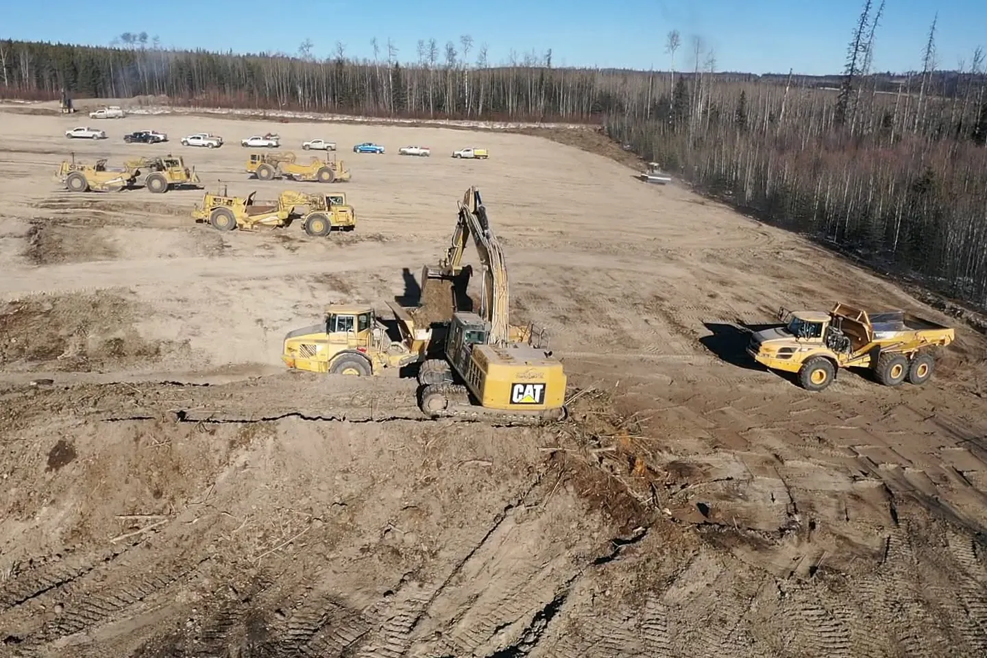 Cat excavator loading a rock truck on a pad with scrapers parked in the background