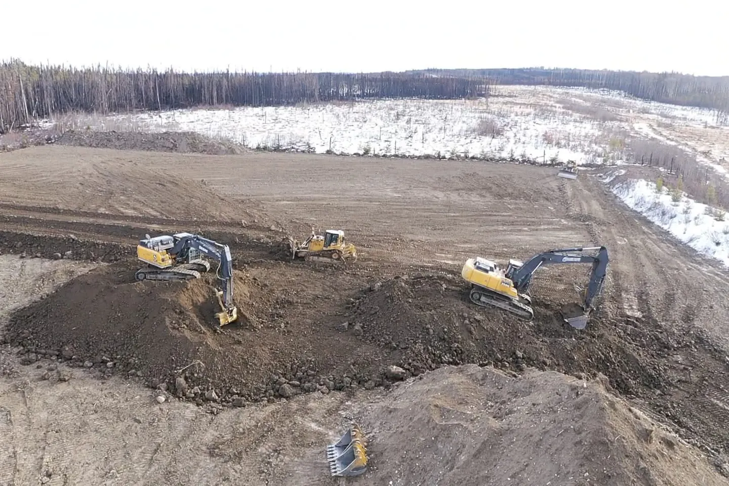 Two excavators and a dozer shaping soil piles on a pad under construction