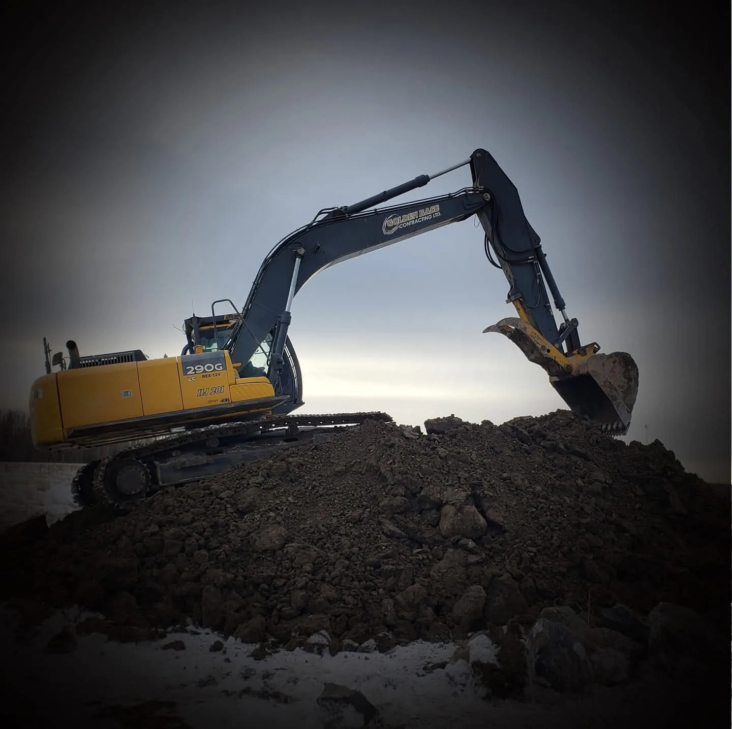 Tracked excavator silhouetted against the sky on a dirt mound at dusk