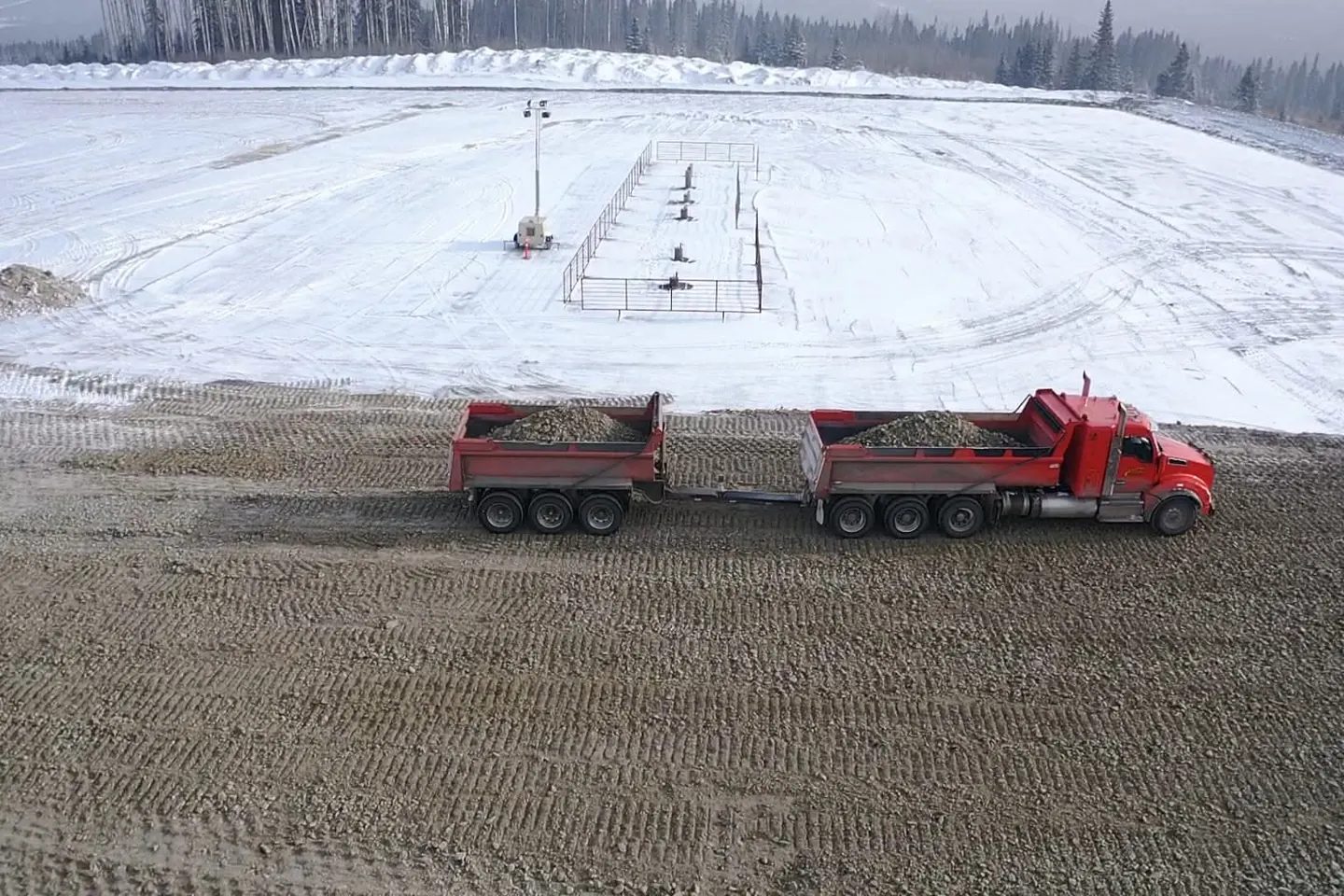 Truck and pup end dump loaded with gravel on a snow covered pad