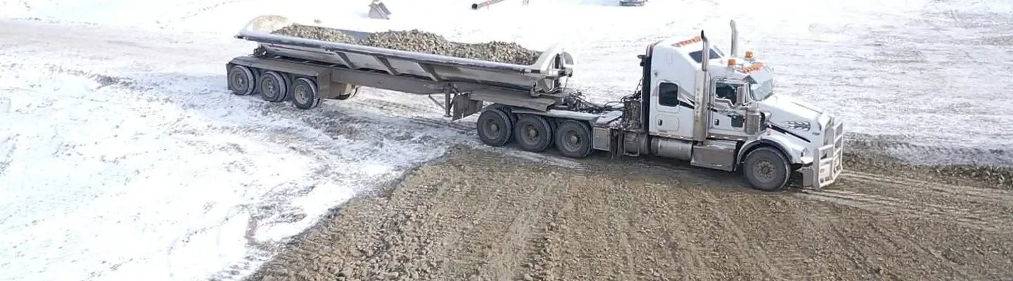 Kenworth tractor and belly dump trailer spreading gravel on a snow covered road