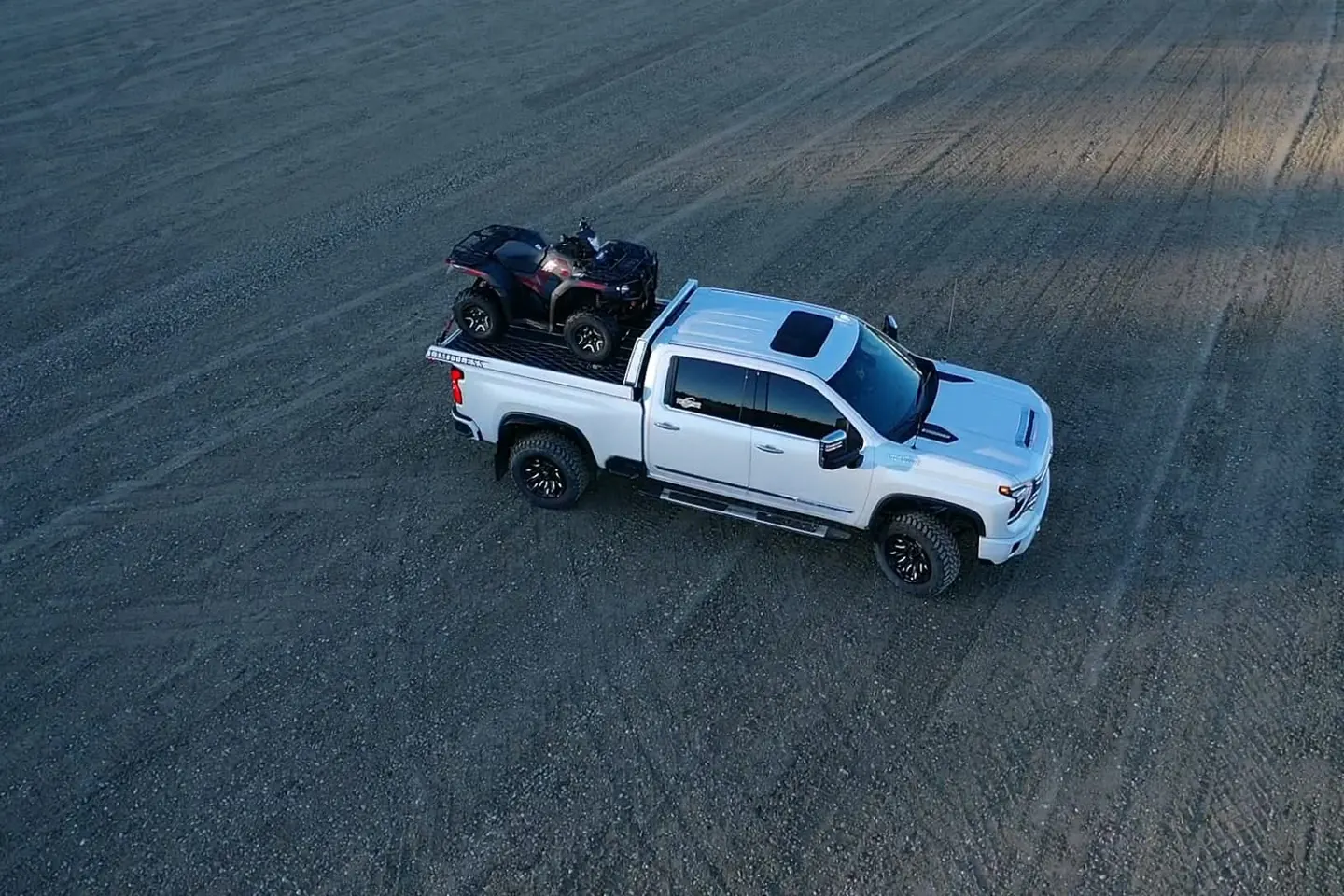 Crew cab pickup with a quad loaded in the box parked on a gravel pad