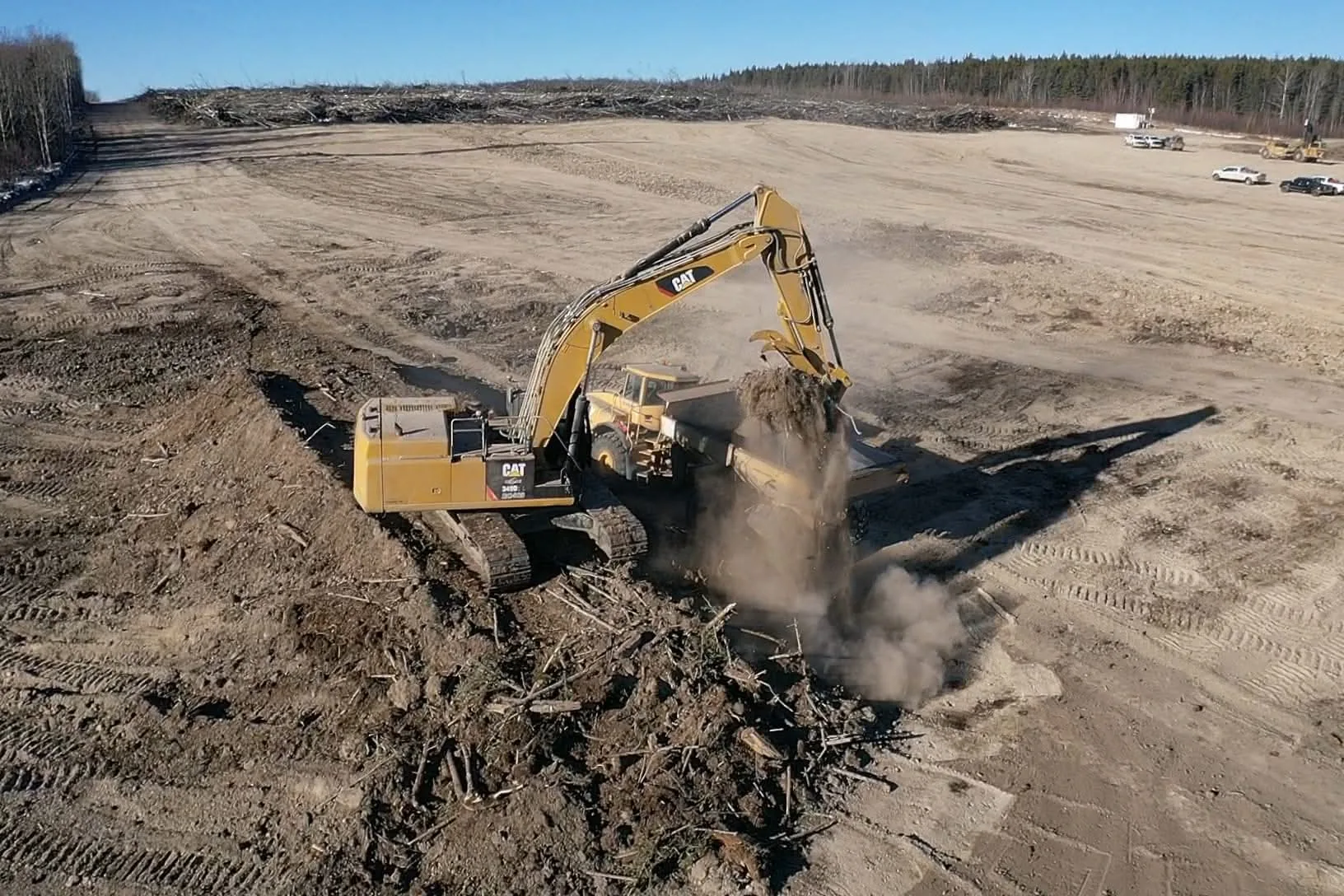 Tracked excavator loading an articulated rock truck on a wide cleared pad
