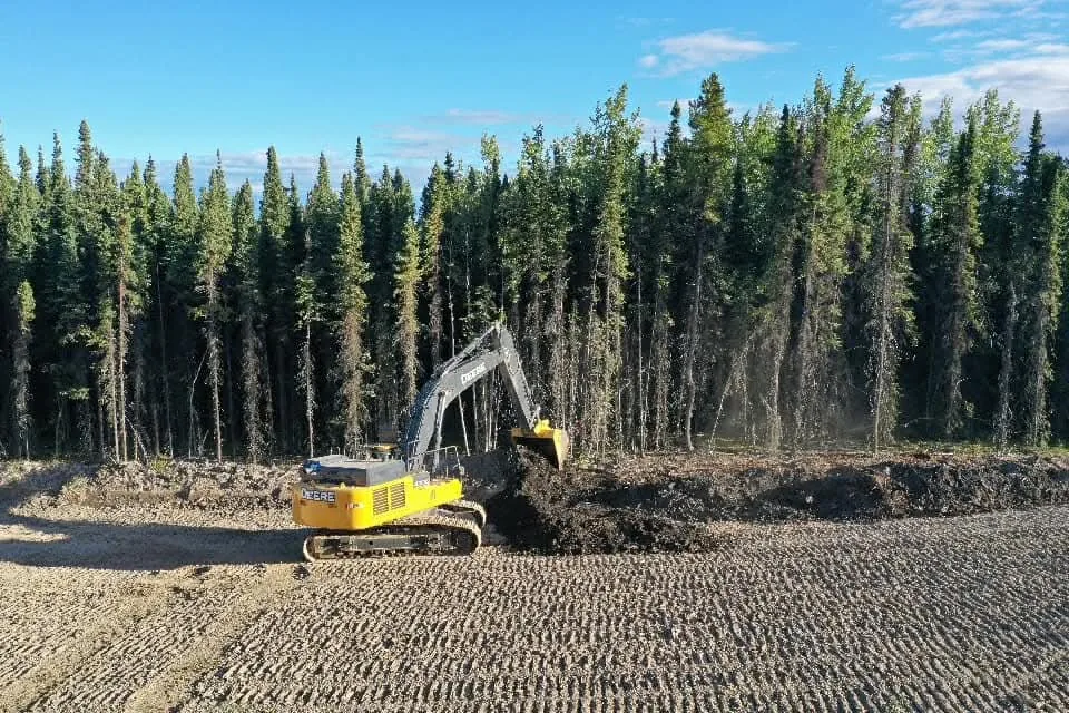 Tracked excavator loading topsoil at the edge of a gravelled lease pad