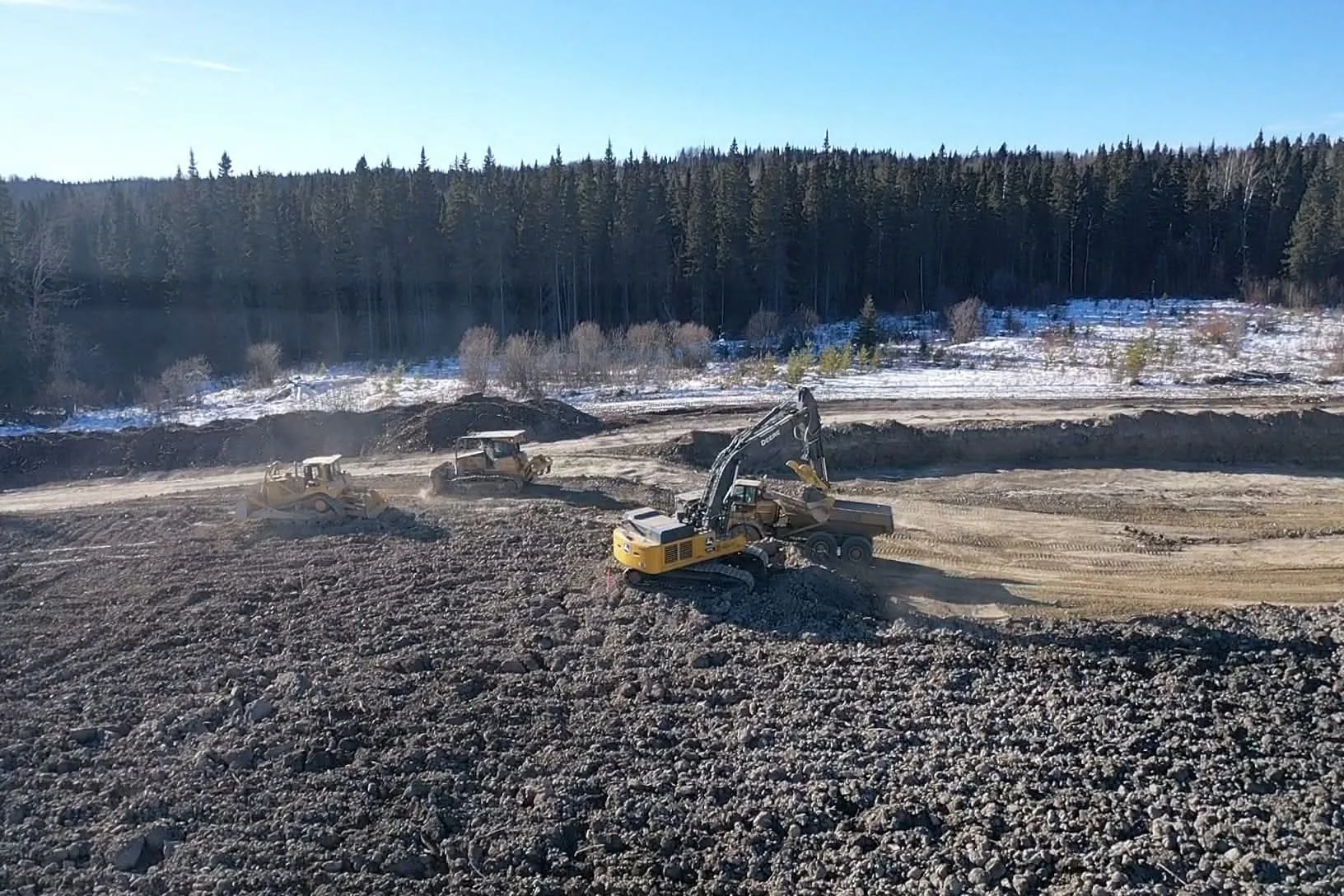 Two dozers spreading fill while an excavator loads a rock truck