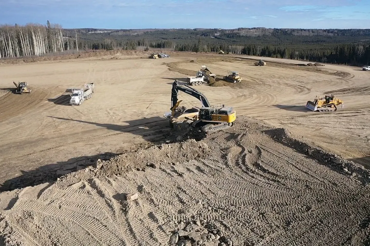 Deere excavator, end dump trucks and dozers spread across a wide dirt pad