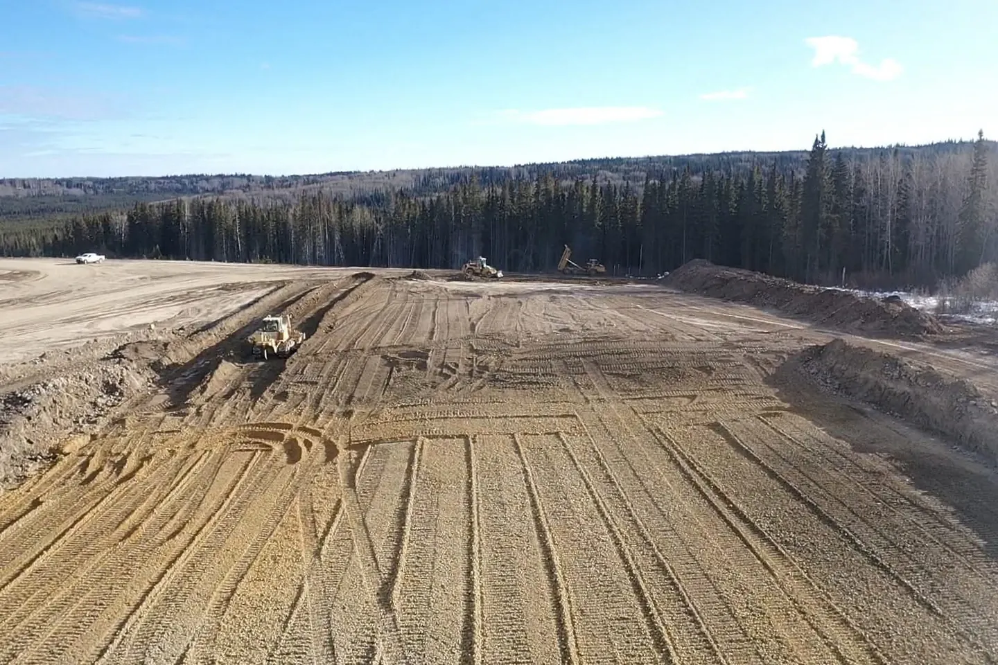 Dozer shaping subgrade on a pad with a rock truck placing fill behind it